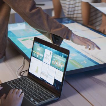 Team collaborating over digital screens and laptop in a modern workspace.