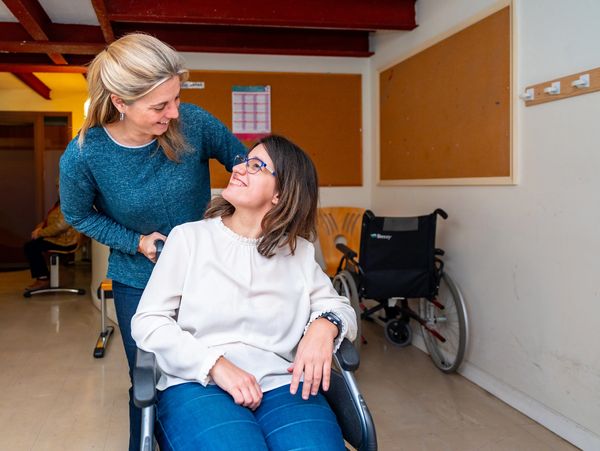 Caregiver smiling at a woman in a wheelchair inside a care facility.