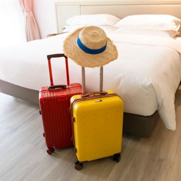 Two colorful suitcases and a straw hat in a bedroom.