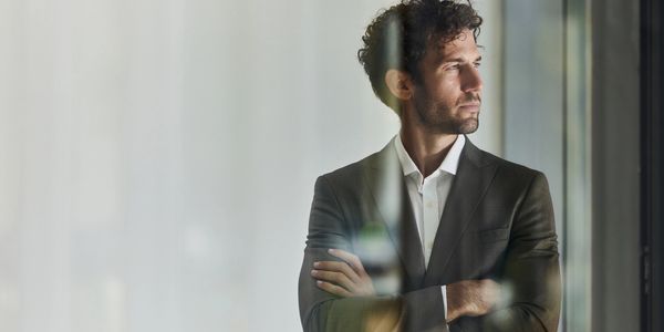 Man in a suit looking thoughtfully out a window.