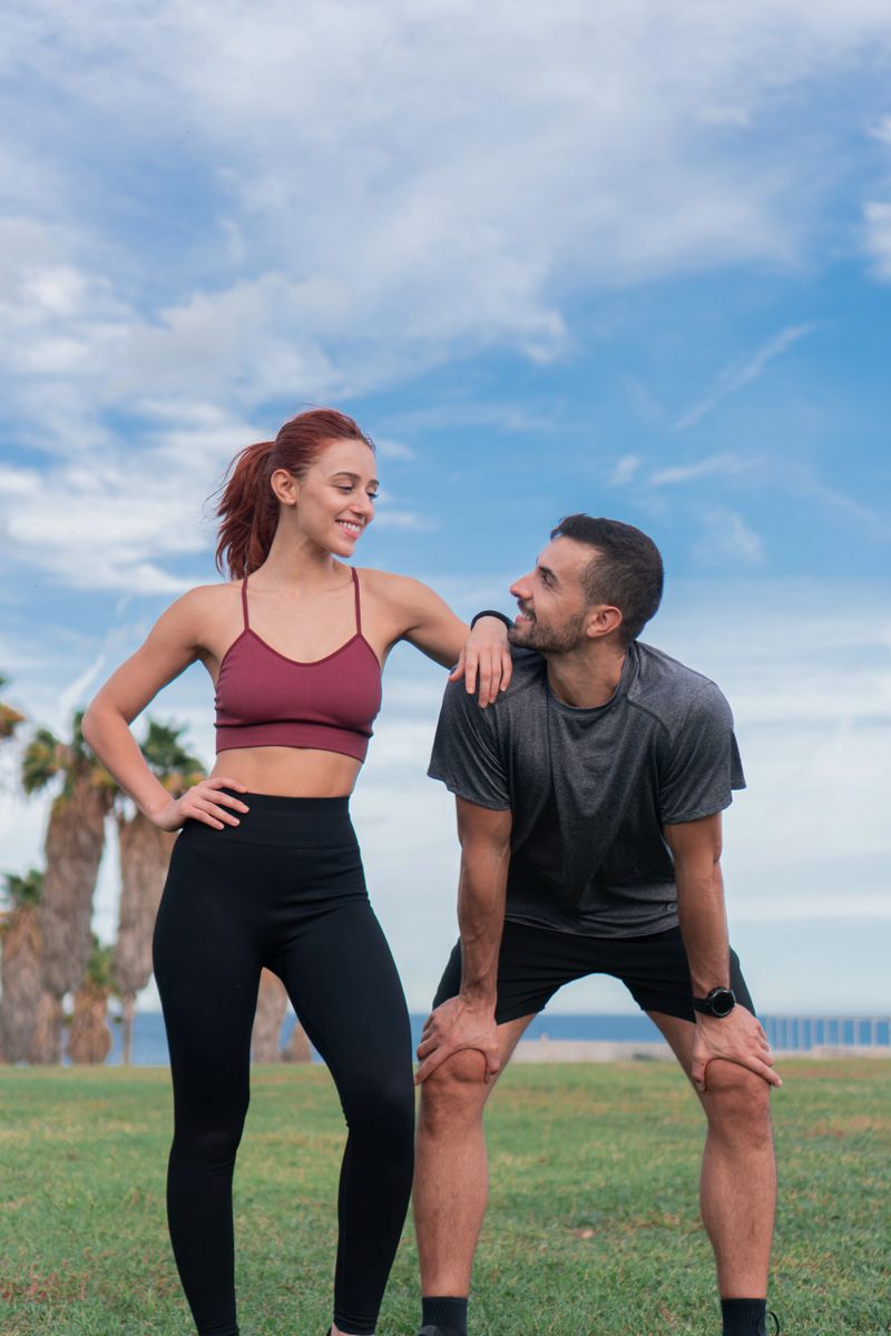 Vertical photo. Young sporty couple male and female resting exhausted with a hard training enjoying wellbeing and healthy lifestyle outdoors. Caucasian man and woman in sportswear relaxing and smiling after working out. High quality photo