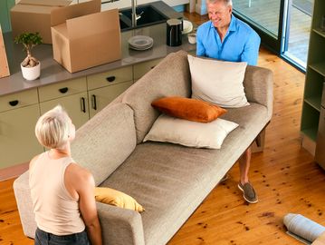 A couple carrying a sofa into a new home with unpacked boxes around.