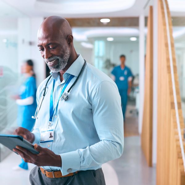 Smiling doctor using a tablet in a hospital corridor.