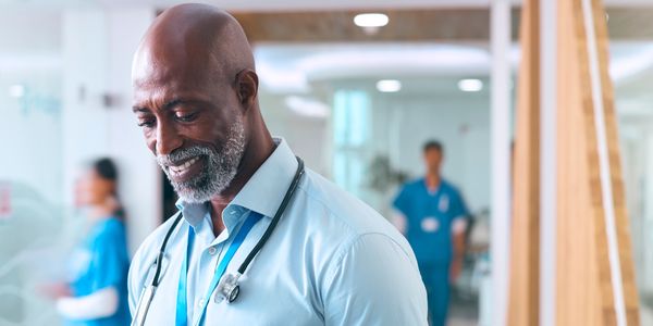 Smiling doctor using a tablet in a hospital hallway.