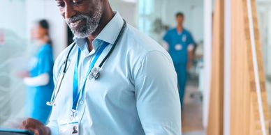Smiling doctor using a tablet in a hospital hallway.