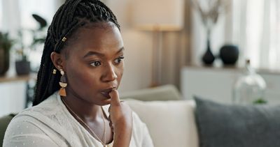Thoughtful woman with braided hair sitting indoors, lost in contemplation.