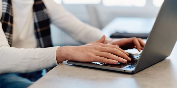 Person typing on a laptop at a table in a bright indoor setting.