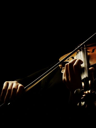 Hands playing a violin in dramatic lighting.