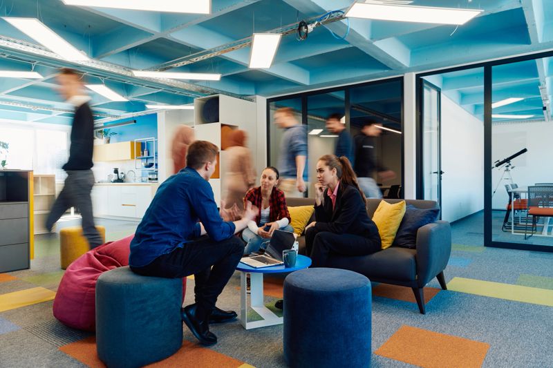 Multiethnic startup business team on meeting in a modern bright open space coworking office. Brainstorming, working on laptop. Group of coworkers walking around in motion blur.