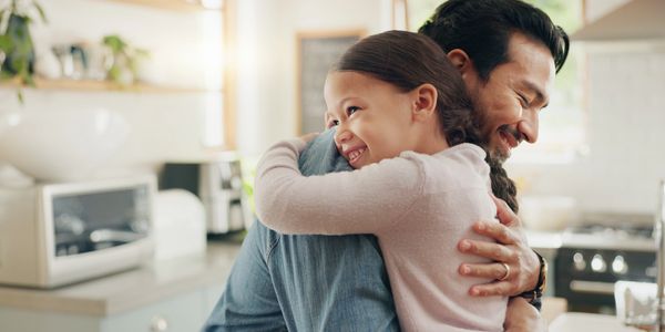 Father giving his young daughter a hug with a kitchen in the background. Both are smiling