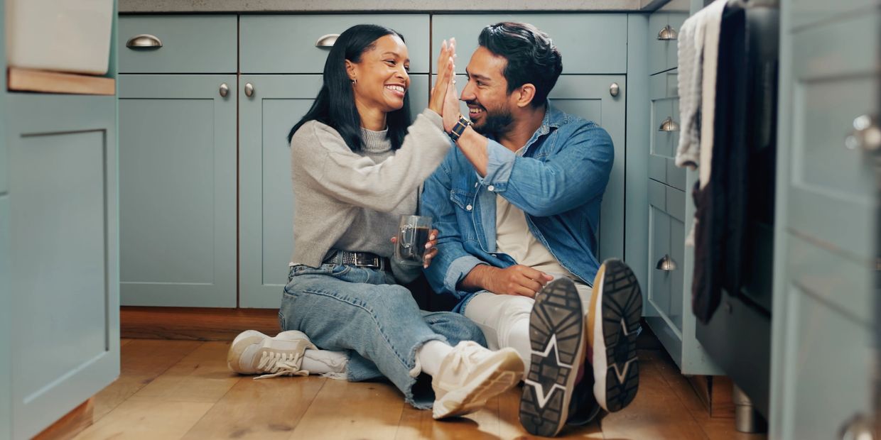 Couple sitting on the kitchen floor giving a high five.