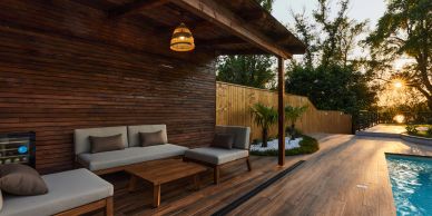 Modern patio with wooden furniture next to a pool at sunset.