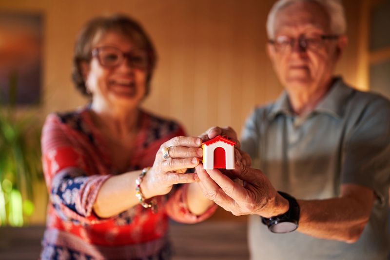 Senior couple holding small house, property concept