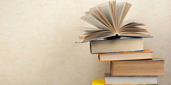 Stack of books with one open on top against a beige background.