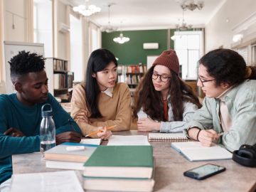 Four diverse students collaborating around a table with books and notes.