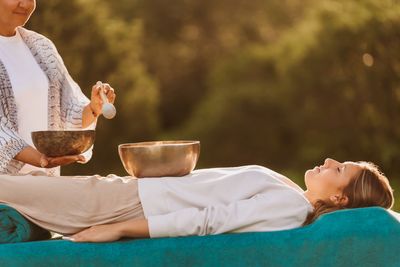 A woman receives a sound healing session outdoors with singing bowls.
