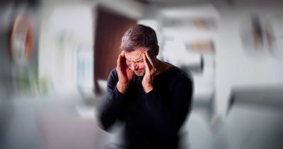 Man holding his head in pain, blurry background.