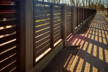 Sunlit wooden fence casting shadows on a brick pathway.