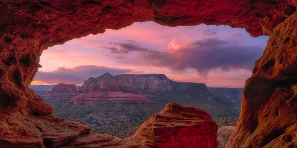 Sunset view from a red rock cave overlooking a valley and mountains.