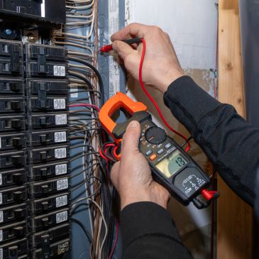 Technician measuring voltage in an electrical panel using a digital multimeter.