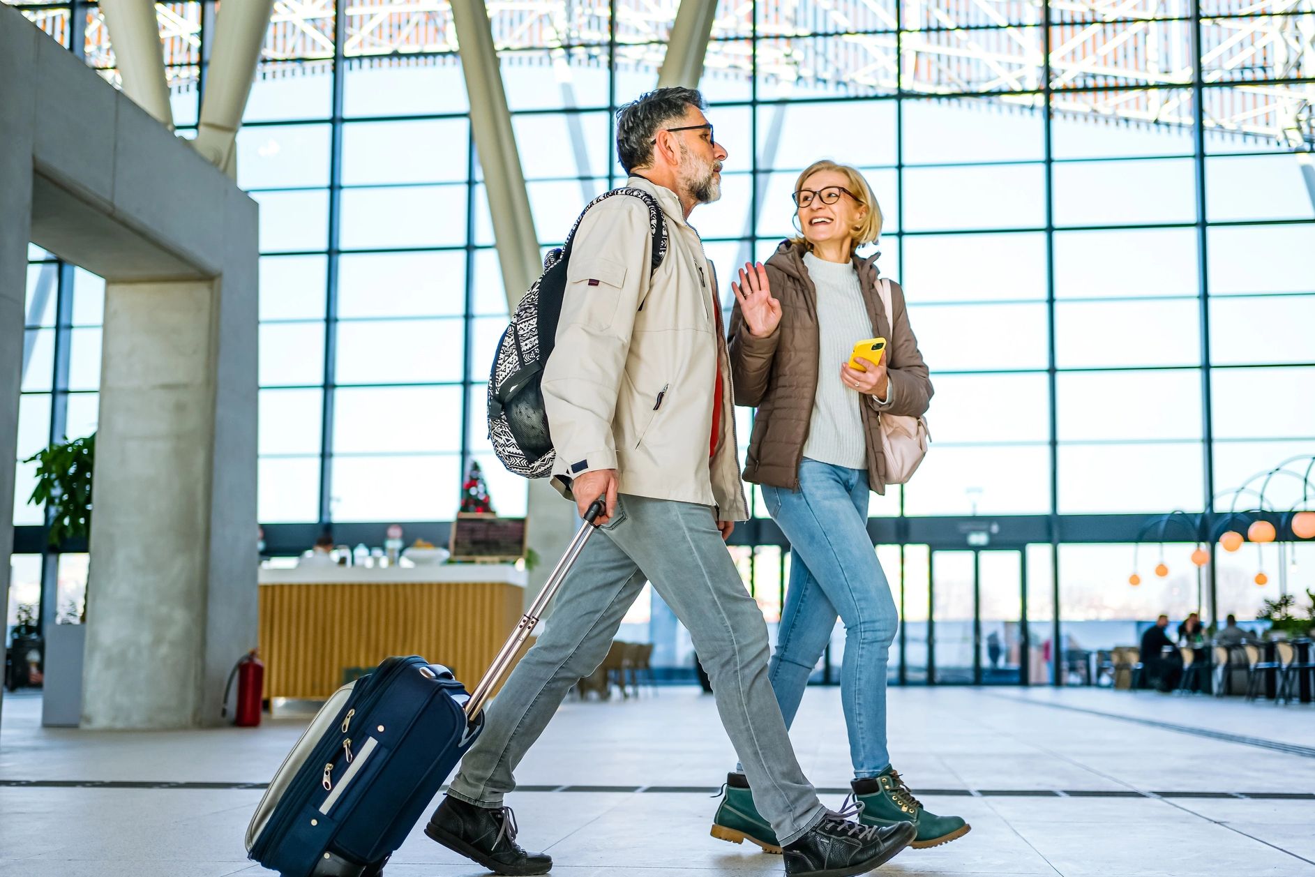 A middle-aged couple walking through an airport with luggage and smiling at each other.