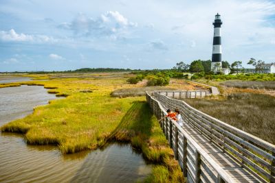Couple walking on wooden boardwalk near a lighthouse.