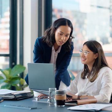 Two women collaborating on a project in an office with a laptop.