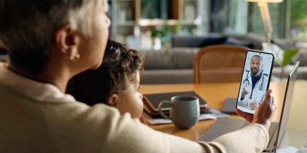 Mother and child in telehealth consultation with doctor on smartphone.