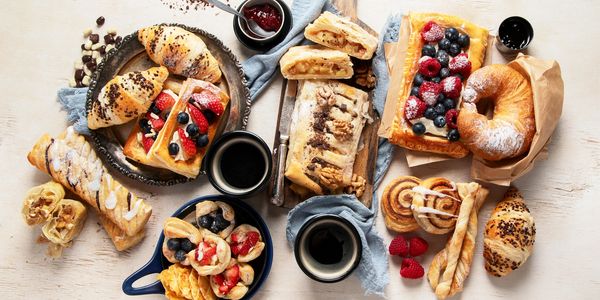 Assorted pastries and coffee cups on a light wooden table.