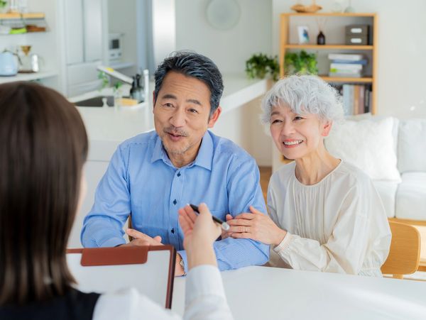 Smiling elderly couple consulting with a professional in a bright, cozy home setting.
