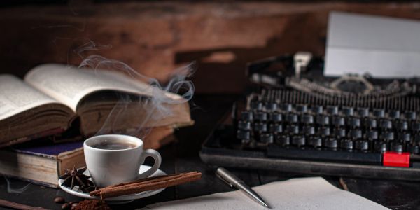 Coffee cup, typewriter, and open book on a desk.