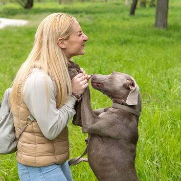 Blonde woman shares a joyful moment with her playful dog in a green park.