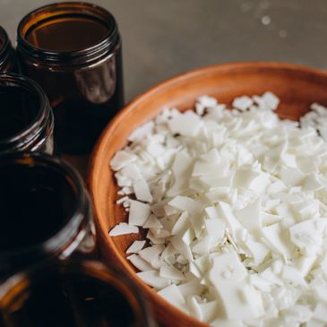 Brown glass jars next to a bowl filled with white wax flakes.