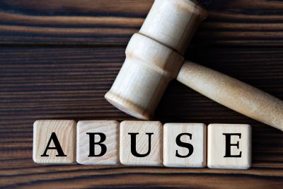 Wooden blocks spelling 'ABUSE' with a judge's gavel on a wooden surface.