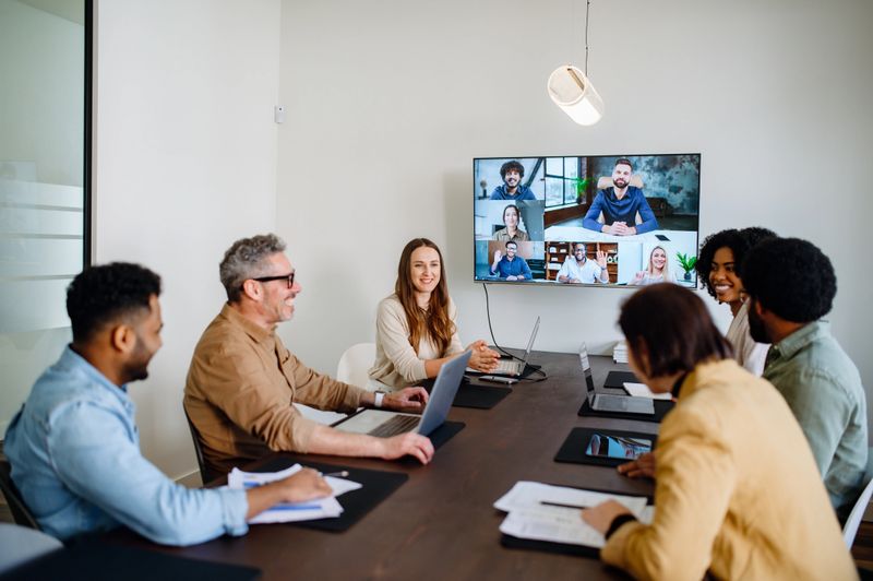 A lively and productive team meeting is captured where colleagues are connected via a large screen, showcasing a blend of in-person and remote collaboration. This image emphasizes the seamless integration of technology in modern business communications.