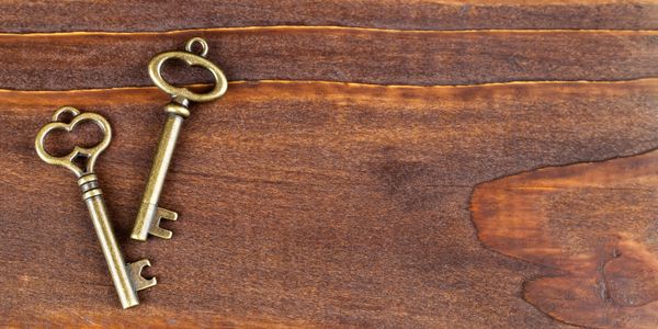 Two vintage brass keys on a wooden surface.