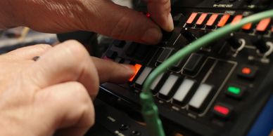 Hands adjusting buttons on an electronic music device with glowing lights.