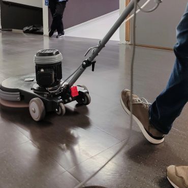 Person cleaning floor with a floor buffer machine.