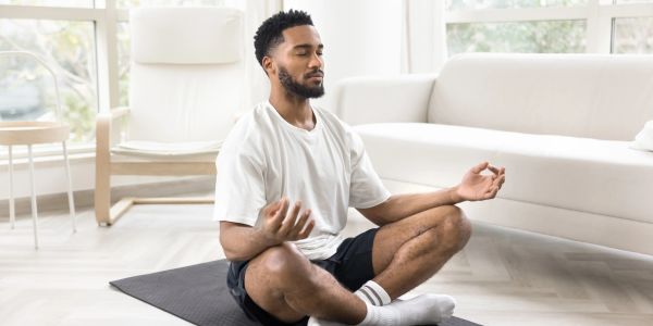 Man meditating cross-legged on a yoga mat indoors.