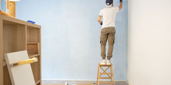 Person painting a wall light blue while standing on a stool.