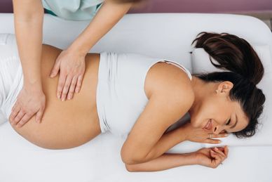 Pregnant woman receiving a gentle belly massage while smiling relaxed.