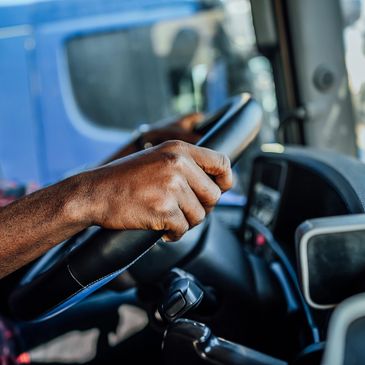 Close-up of a truck driver gripping the steering wheel inside a vehicle cabin.