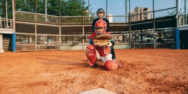 Two young baseball players in catching gear ready behind home plate on a sunny day.