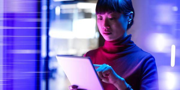 Woman using a tablet under neon blue and purple lighting.