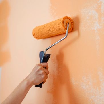 Person painting a wall orange with a paint roller.