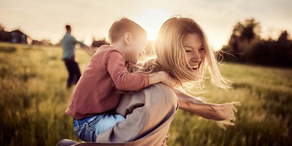 Child riding piggyback on a woman in a field.