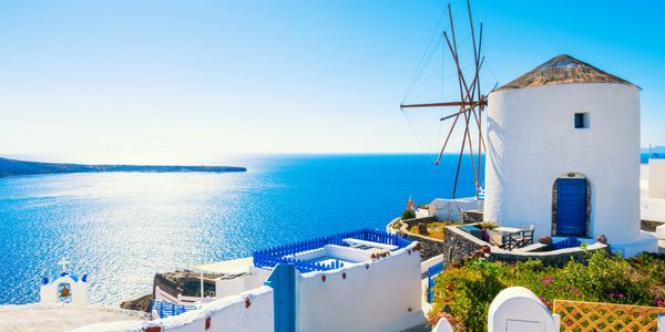 A traditional white windmill overlooking the blue sea in a sunny coastal village.