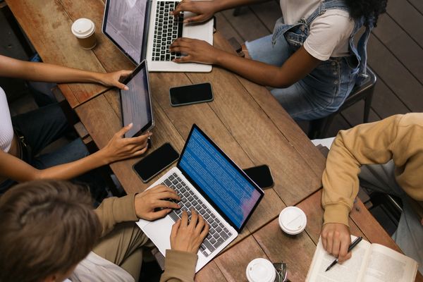 A group of diverse young adults studying together with laptops, tablets, and books.