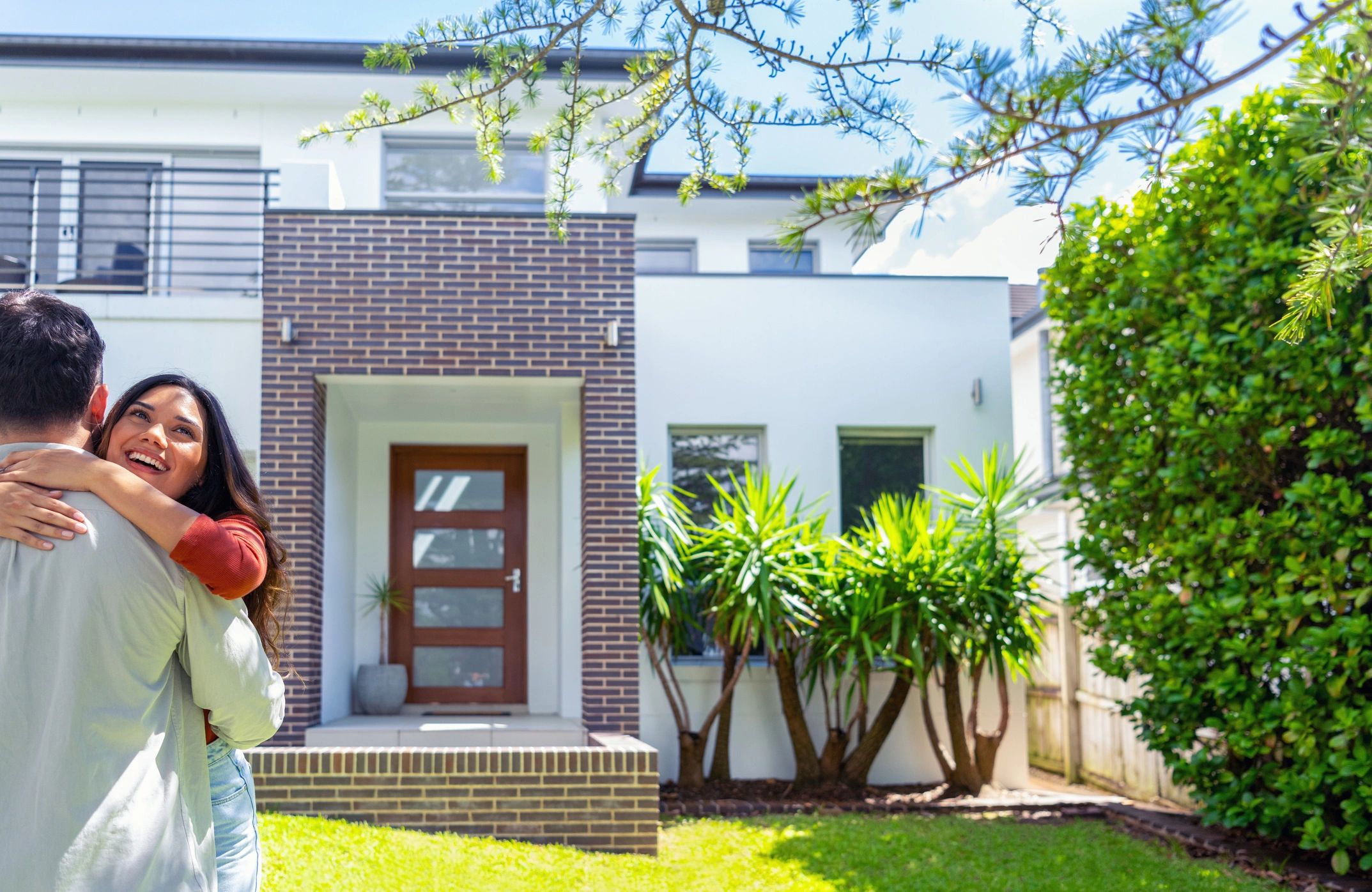 Happy couple embracing outside their modern home on a sunny day.