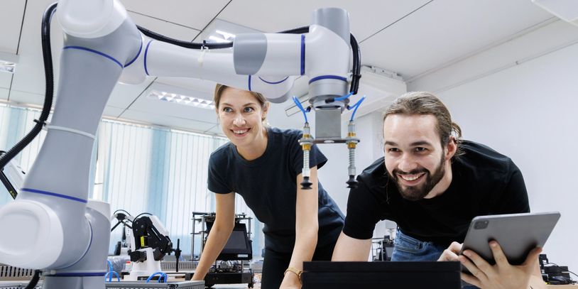 Two engineers smiling while working with a robotic arm in a modern lab.